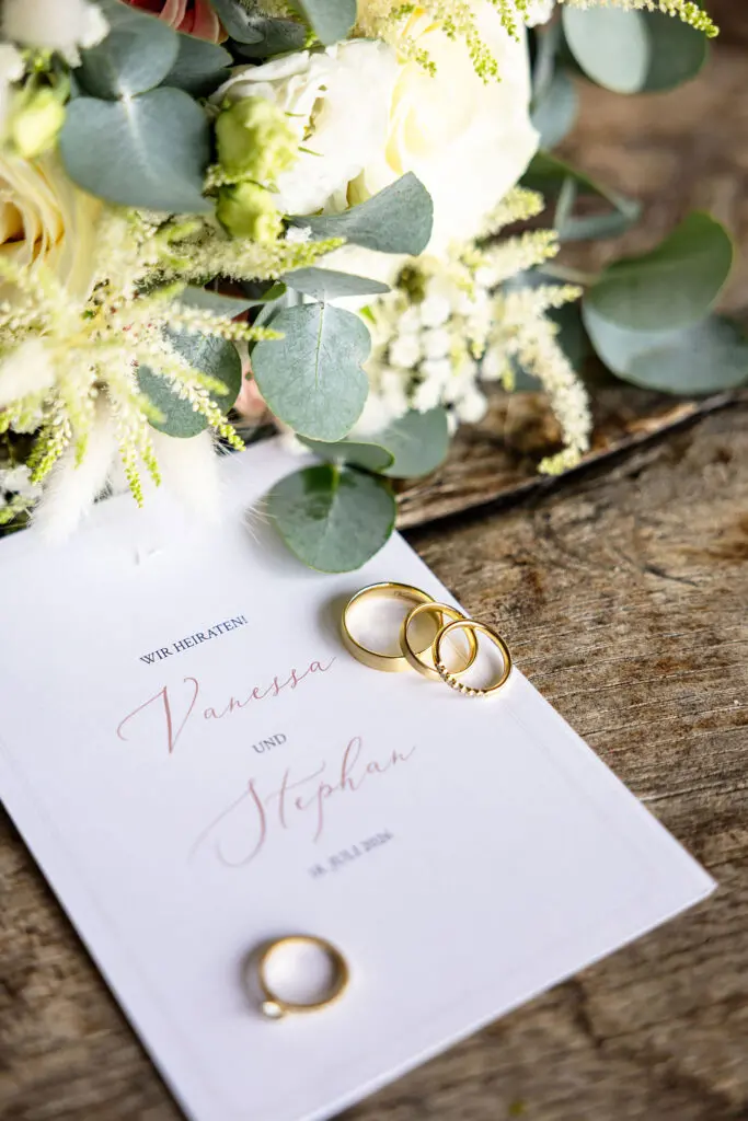 Eheringe, Hochzeitseinladung und Brautstrauß als Detailaufnahme bei einer Hochzeit