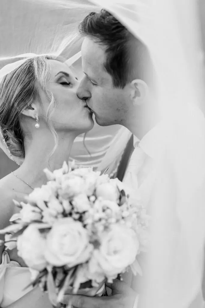 Braut und Bräutigam küssen sich bei ihrer Hochzeit auf der Turracher Höhe, mit Blumenstrauß und Schleier